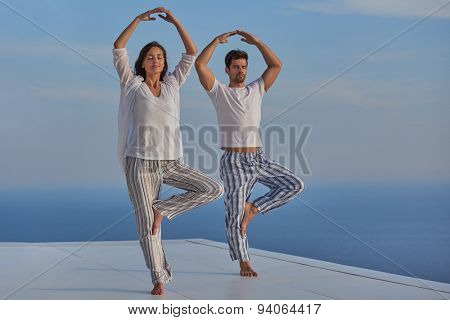 young couple practicing yoga at sunset in modern home terace with ocean and sunset in background