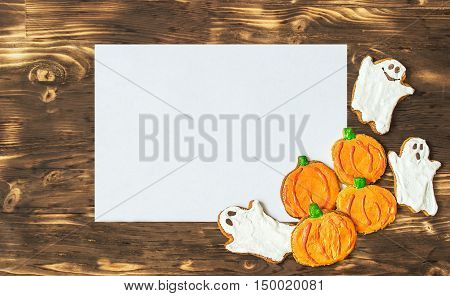 Funny delicious ginger homemade biscuits for Halloween on the dark wooden table with sheet of papper as a space for text. horizontal view from above. Halloween cookies