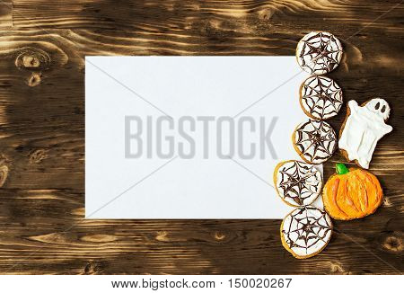 Funny delicious ginger homemade biscuits for Halloween on the dark wooden table with sheet of papper as a space for text. horizontal view from above. Halloween cookies