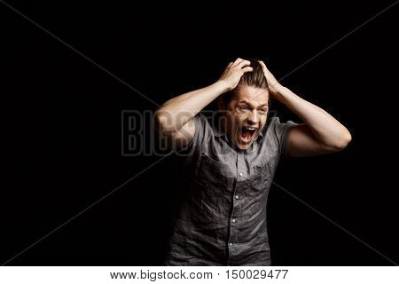Dissapointed young handsome man grab his head, shouting over black background. Copy space.