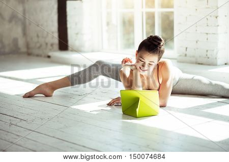 Take a break. Attractive nice professional dancer looking at the tablet and smiling while doing the splits