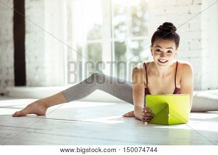 Pleasurable relaxation. Pretty skillful female dancer holding her tablet and smiling while taking a break during a workout