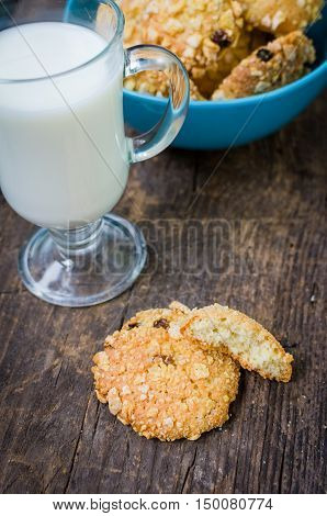 Homemade cornflakes and raisins cookies with cup of milk on old wooden table. Freshly baked corn flake cereal cookies on rustic background. Selective Focus.