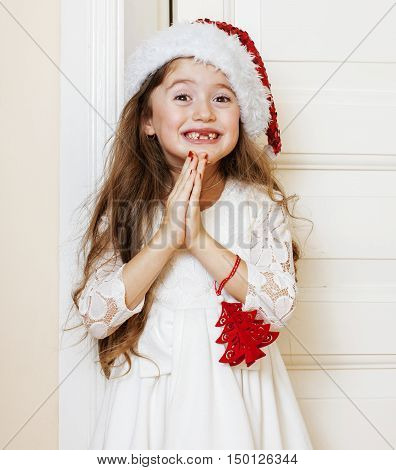 little cute girl in santas red hat waiting for Christmas gifts. smiling adorable kid. White new dress home interior close up