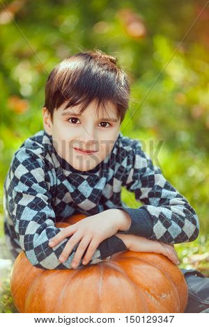 Boy Resting on a Pumpkin on green grass and autumn leaves