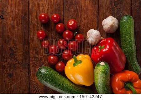 Heap of fresh organic tasty vegetables on brown wood background for menu or recipe. Healthy natural food on wooden table. Bright peppers and other cooking ingredients above view