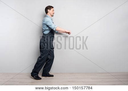Work with enthusiasm. Pleasant senior deligent man holdign truck and workign while walking along grey wall