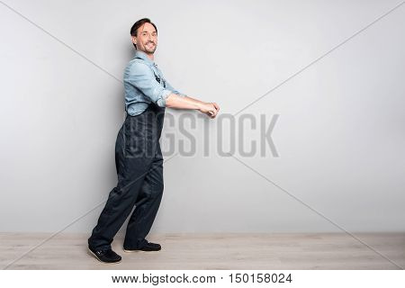 Real worker. Pleasant delighted diligent man holdign truck and smiling while standing isolated on grey background