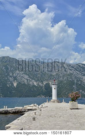 The artificially created island Our Lady of the Rock island in Kotor Bay Montenegro. A small oleander plant can be seen in the foreground and a small lighthouse in the background