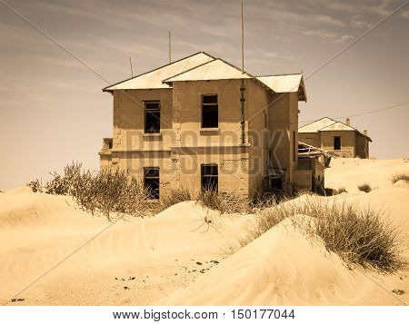 Ghost buildings of old diamond mining town Kolmanskop near Luderitz in Namibia. Abandoned house ruins sunken in the sand dunes of Namib Desert. Vintage toning photography.