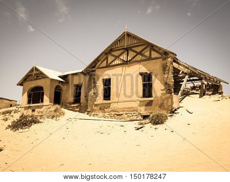 Ghost buildings of old diamond mining town Kolmanskop near Luderitz in Namibia. Abandoned house ruins sunken in the sand dunes of Namib Desert. Vintage toning photography.