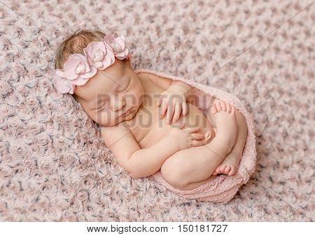 lovely newborn curled up asleep, wrapped in pink diaper on knitted blanket