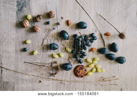 lying on wooden background grapes plums dry grassthistlewalnuts biscuit.layflat