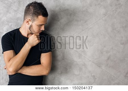 Side view of handsome caucasian man in black T-shirt on textured concrete wall background