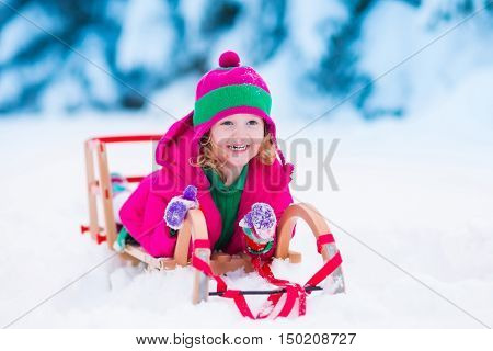 Little girl enjoying a sleigh ride. Child sledding. Toddler kid riding a sledge. Children play outdoors in snow. Kids sled in the Alps mountains in winter. Outdoor fun for family Christmas vacation.