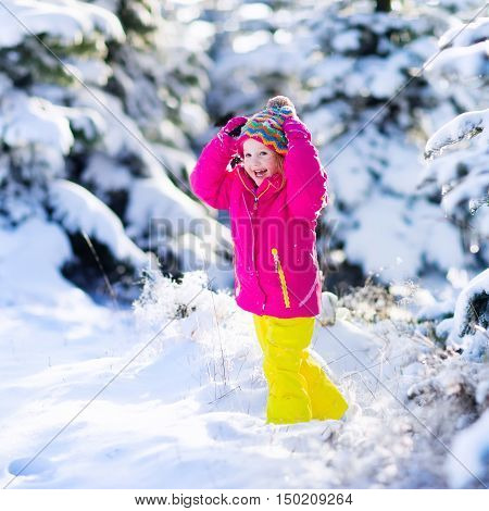 Child running in snowy forest. Toddler kid playing outdoors. Kids play in snow. Christmas vacation in sunny winter park for family with young children. Little girl in colorful jacket and knitted hat.