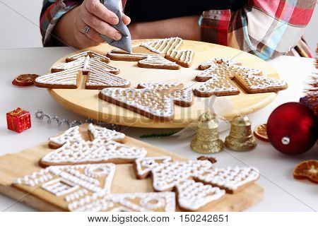 Woman decorating gingerbread cookies in the shape of Christmas tree. Close up view with selective focus.