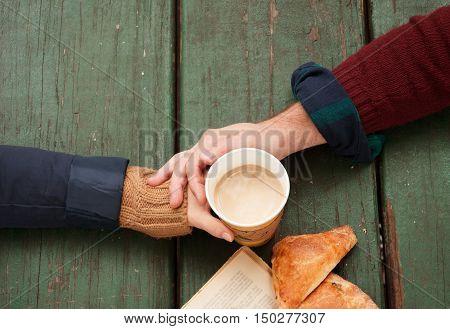 Man holds woman's hand with cup of coffee top view image on wooden autumn background.