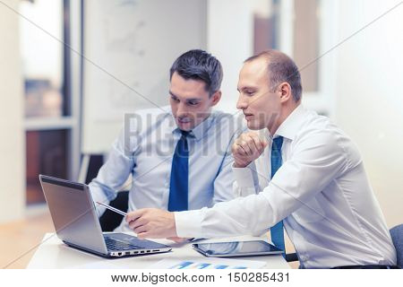 business, technology and office concept - two businessmen with laptop, tablet pc computer and papers having discussion in office