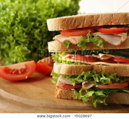Enorme sanduíche com presunto fresco, salada, pepino e tomate. Profundidade de campo.