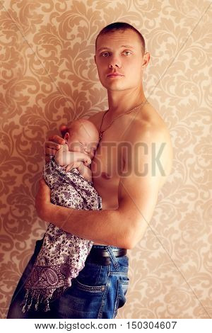 Young strong man holding a small fragile baby in her arms. Athlete bodybuilder posing with newborn son
