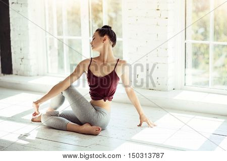 Concentrated on it. Young beautiful flexible girl having her morning training in a gym and doing yoga asana.
