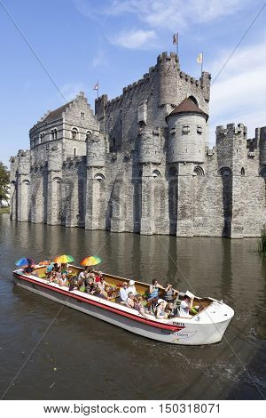 Ghent, 27 august 2016: tourist boat full of colorful people on river near Gravenstein Castle in belgian medieval city centre of Ghent