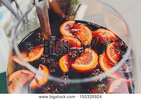 Making hot alcohol, mulled wine for sale at country fair. Glintwine from red wine with citrus and cloves in big glass, mixed with soup ladle. Closeup