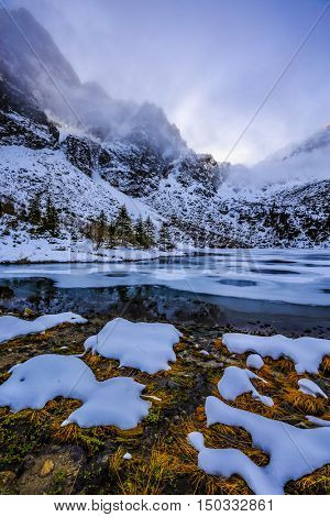 Winter day in Polish Tatra mountains, frozen Morskie Oko lake and summits in the clouds.