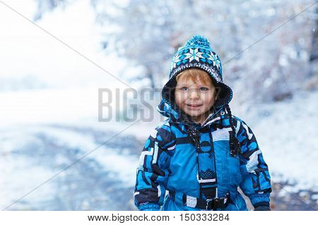 Winter portrait of kid boy in colorful clothes, outdoors during snowfall. Active outoors leisure with children in winter on cold snowy days. Happy toddler child having fun with snow in forest