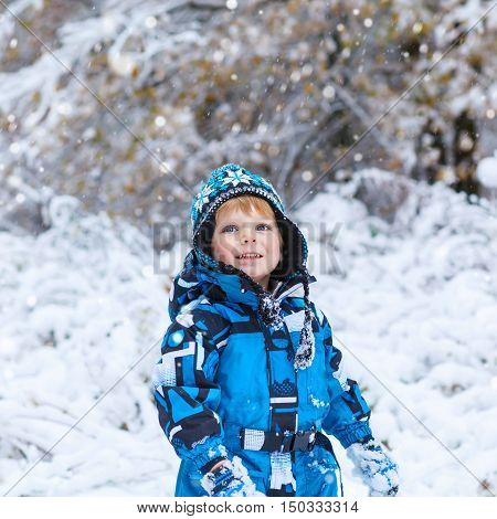 Winter portrait of kid boy in colorful clothes, outdoors during snowfall. Active outoors leisure with children in winter on cold snowy days. Happy toddler child having fun with snow in forest