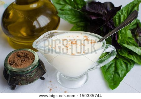 Classic European white sauce Bechamel in saucer with nutmeg, basil and olive oil on white background. Bechamel sauce for traditional European dishes. Italian food concept. Selective focus.