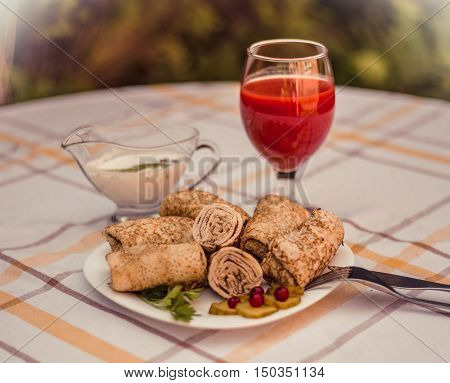 Tasty pancakes with meat on white plate closeup. Crepes stuffed with finely cut meat. glass of tomato juice and white sauce.