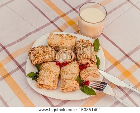 Tasty pancakes with home made cheese on white plate closeup. Crepes stuffed with cheese, and glass of milk on checked table cloth.