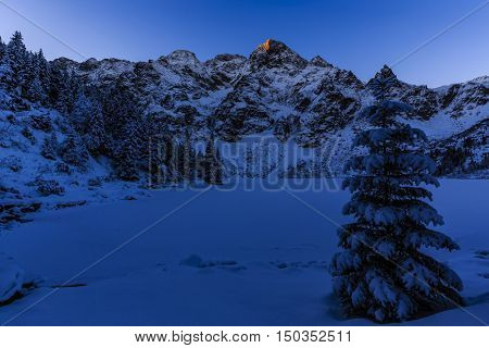 Winter night in Polish Tatra mountains, frozen Morskie Oko lake and summits in first morning sun rays.