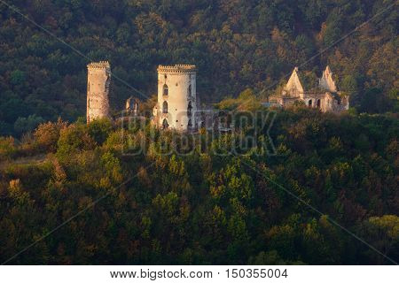 Sunlit ruins of Chervonohorod Castle against autumn trees background.