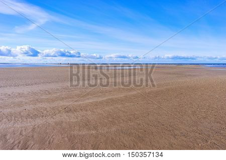 People walk in a day on a wide yellow sandy beach at low tide in the Baltic Sea in spring