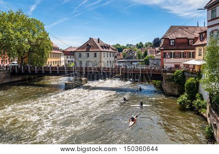 Bamberg Germany - May 22 2016: Tourists on a bridge and canoe slalom on the River Regnitz Bamberg Bavaria Germany Europe. The historic city center is a listed UNESCO world heritage site.