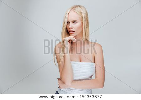 Portrait of a pensive thougtful pretty blonde girl thinking about something isolated on the gray background