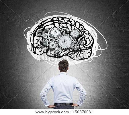 Rear view of man in white shirt standing against blackboard with brain sketch and gears on it. Concept of brain and behaviour studying