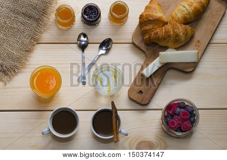 Breakfast for two coffee orange juice water with lemon berries and croissants with different jam on wooden background.Top view