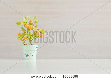 Closeup artificial orange plant with orange fruit in green pot on blurred wooden desk and wall textured background in office room for decorate under window light with copy space