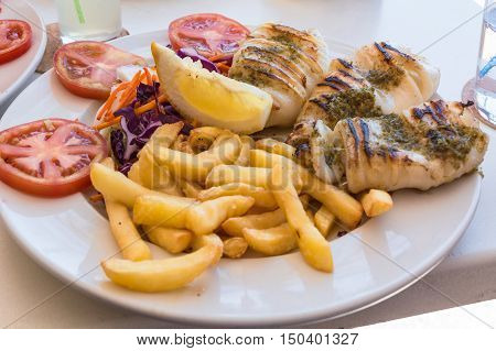 Grilled octopus. Grilled squid served with french fries and lemon and salad.
