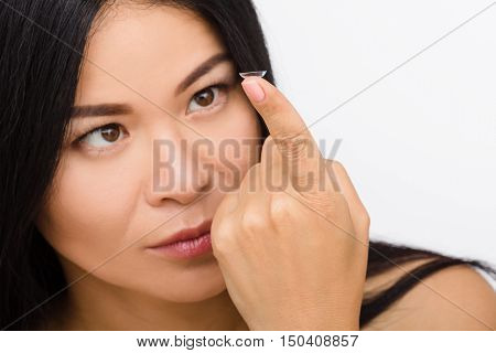 Closeup picture of pretty Korean or Asian woman looking at contact lens isolated on white background. Beauty, vision, eyesight, ophthalmology and people concepts.