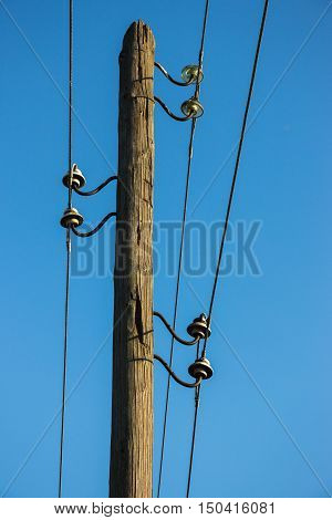 Old wooden pillar with power line against the blue sky