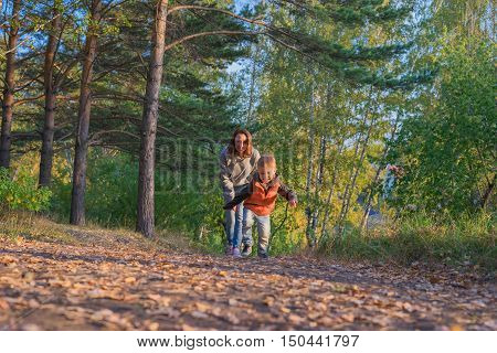 Mother and son running on path in autumn forest. Family at nature autumn bright sunny day fallen yellow leaves underfoot.