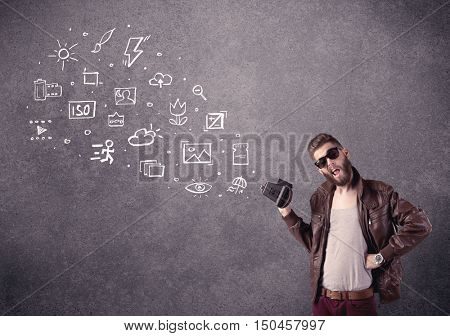 An elegant hipster guy trying to use a vintage camera with camera settings icons drawn on wall, like flash, white balace or ISO value concept