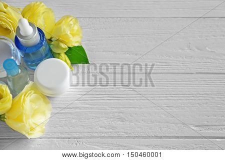 Cosmetic bottles and eustoma flowers on light wooden background
