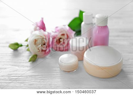 Cosmetic bottles and eustoma flowers on light wooden background