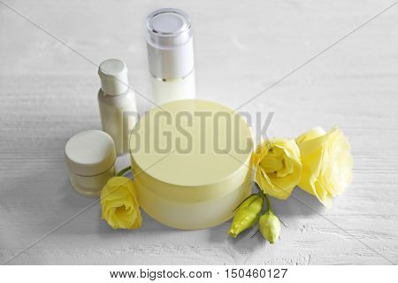Cosmetic bottles and eustoma flowers on light wooden background